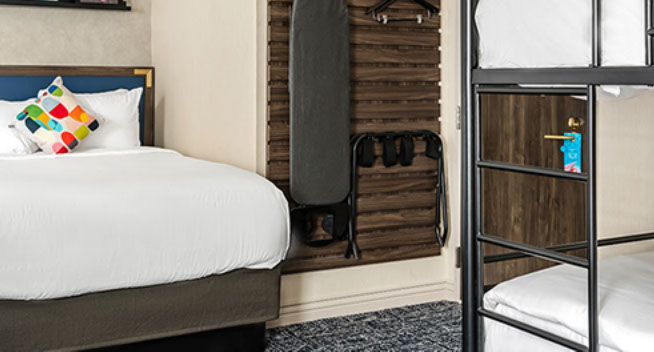 King Bed showing ironing board hanging on wall with lsuitcase rack and clothes hanger