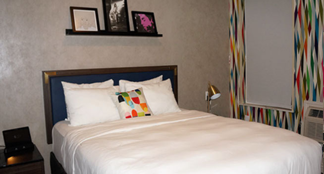 Full Bed Guest room showing full size bed, night stand, lamp, and Aavago communication device.