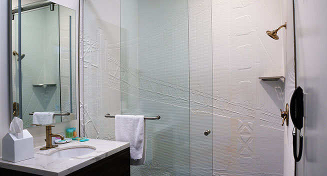 Guest room showing bathroom with double glass shower doors, brass colored fixtures, sink and mirror. Phone in bathroom for your convenience.