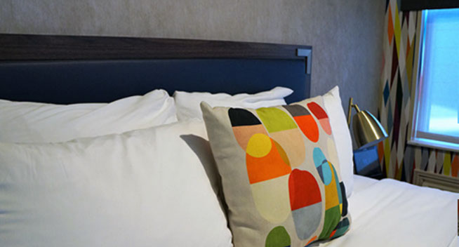 Close up of Full size bed, colorful throw pillow and large window looking out over city of San Francisco.